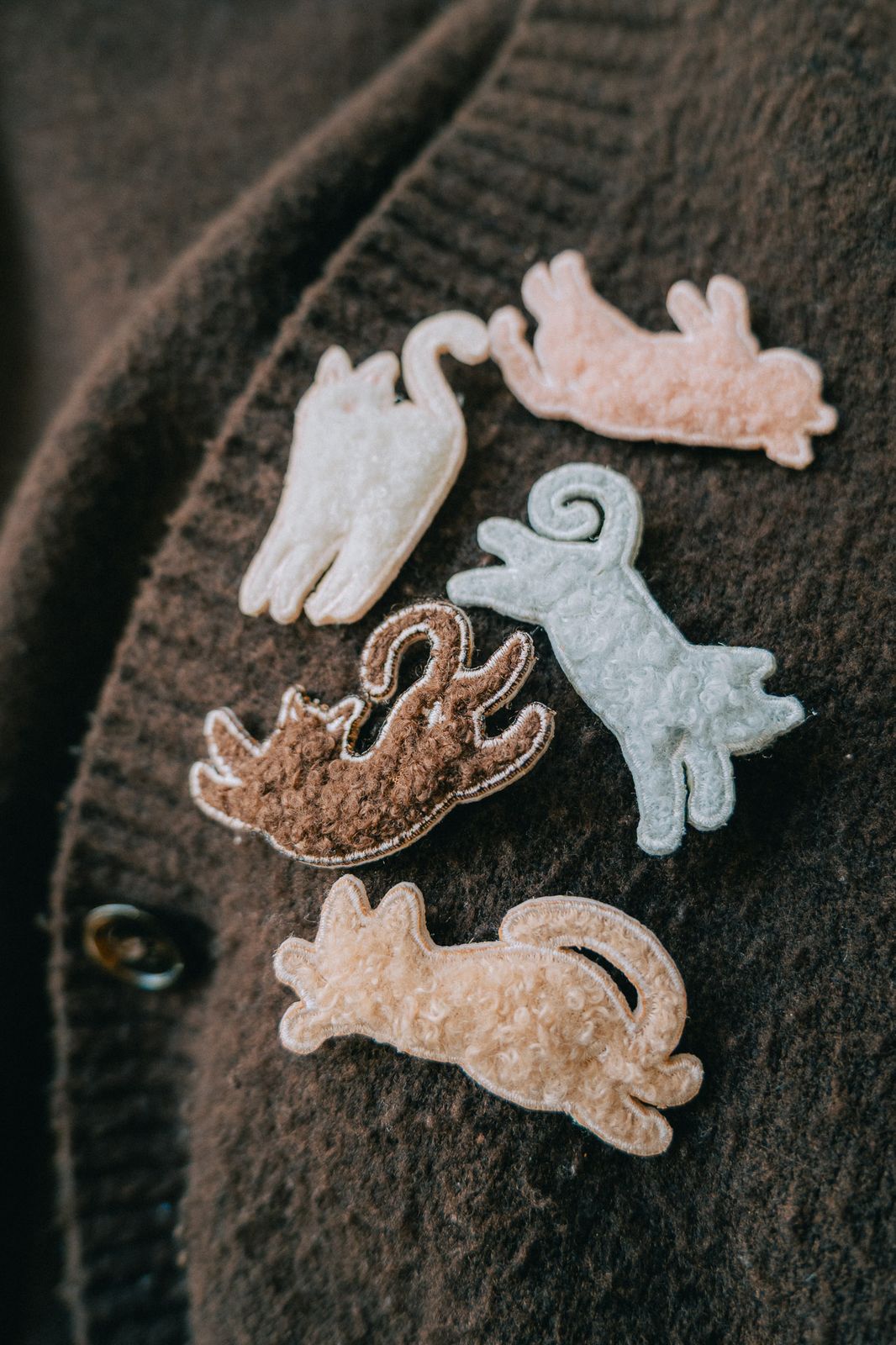 Embroidered cat pins with plush texture on a brown fabric background.